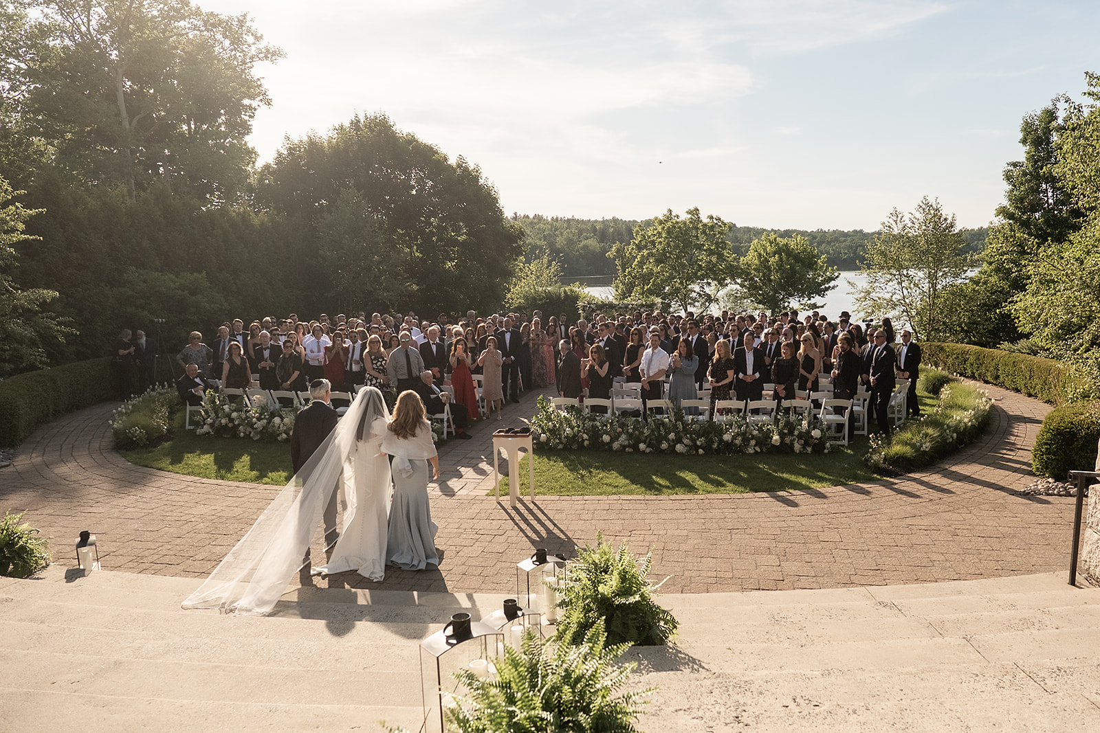 A couple faces their wedding guests at an outdoor ceremony beside a lake